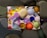 A collection of colorful, abstract shapes fills the frame, featuring a variety of textures and forms. The composition includes soft, fabric-like materials alongside smooth and metallic surfaces, arranged in an artistic, chaotic manner.