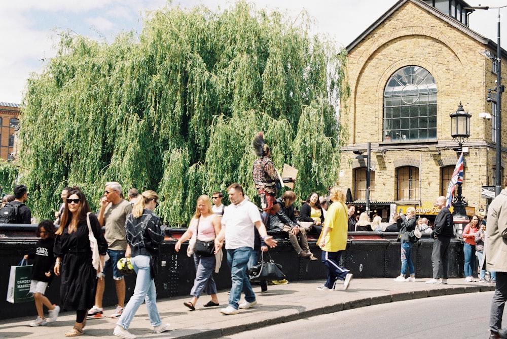 a group of people walking on a sidewalk next to a large tree