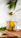 Smiling woman enjoying a spoonful of golden infused honey at a sunny kitchen table.