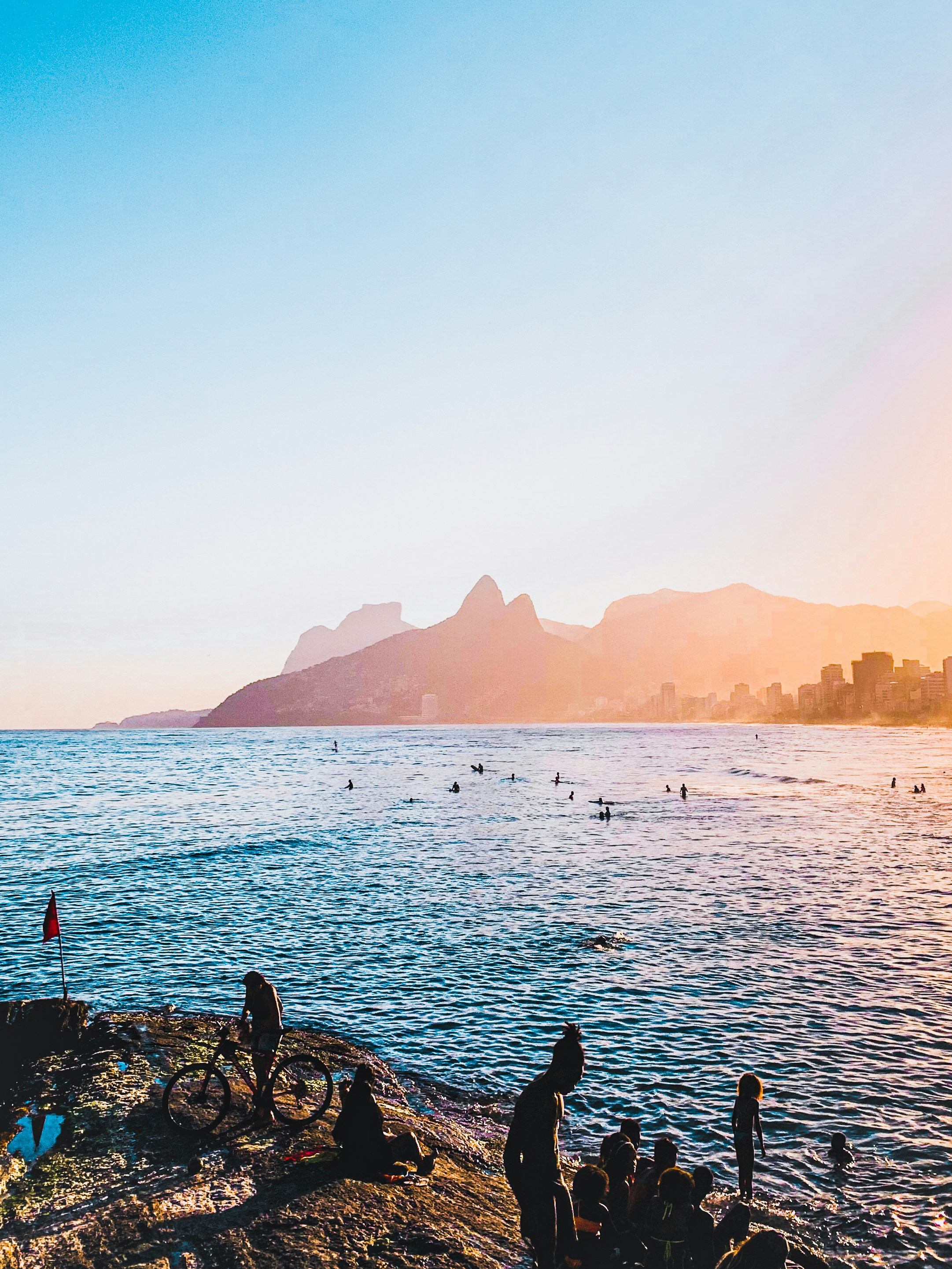People relax by the ocean at sunset with mountains.
