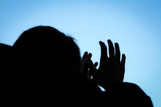 A silhouette of a person is seen against a bright blue background, with their hands raised and fingers slightly spread.