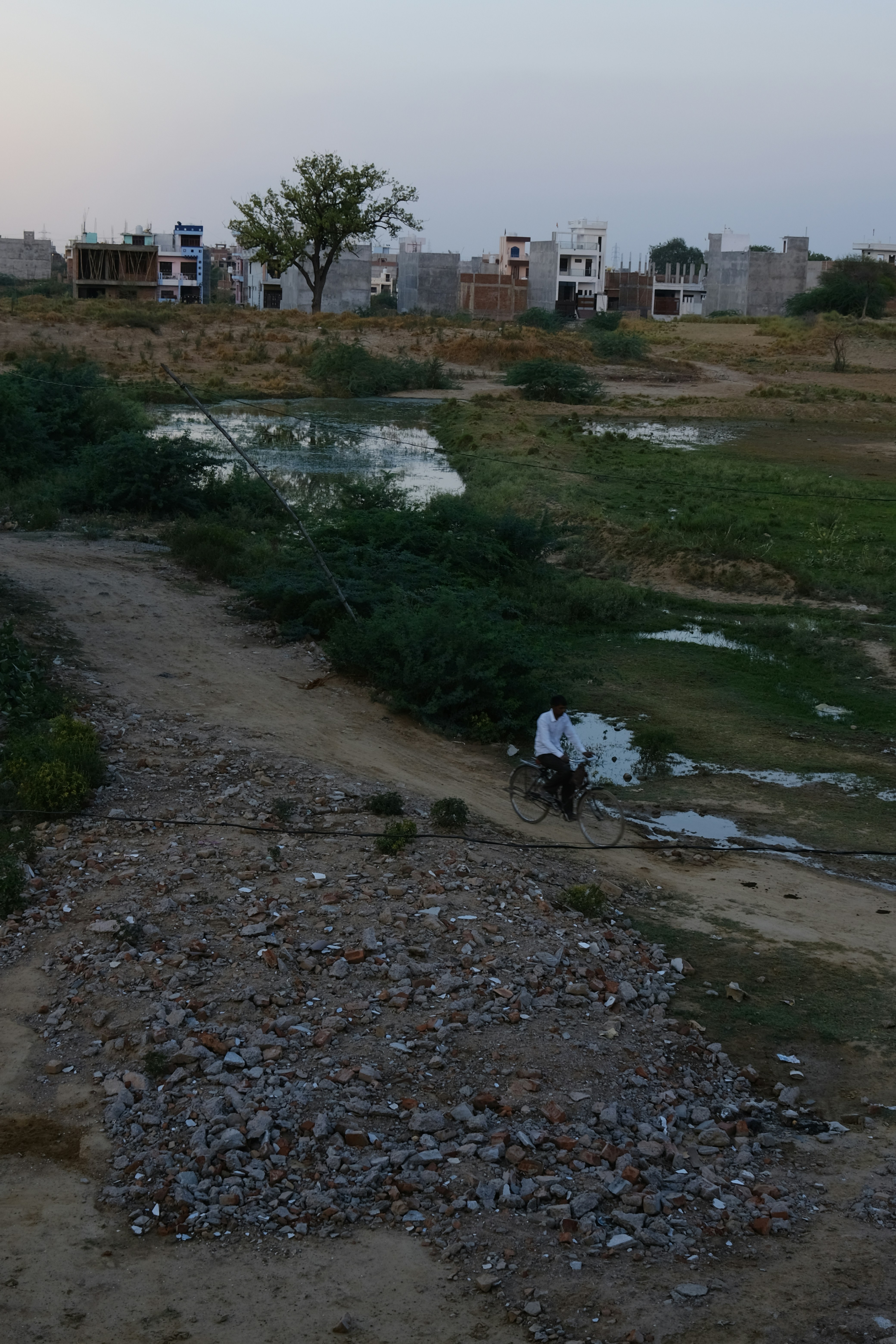 a person riding a bicycle on a dirt path with buildings in the background