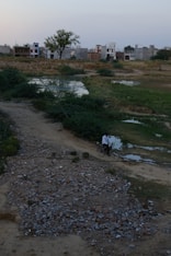 a person riding a bicycle on a dirt path with buildings in the background