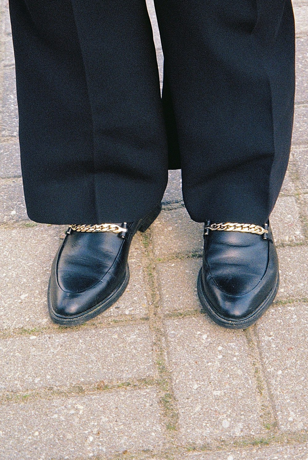 a person's legs wearing black shoes and a gold ring