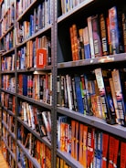 Rows of bookshelves are filled with a variety of colorful books, organized neatly. Some books are titled visibly with genres like mystery and suspense, and they are packed tightly together on metal shelves.