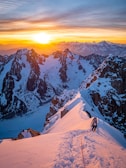 Climber reaching the summit of a snowy Alpine peak at sunrise.