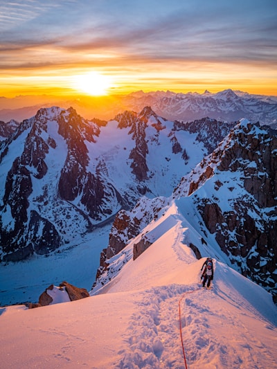A climber reaching the snowy summit of a high Alpine peak at sunrise.