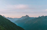 A panoramic view of a misty mountain range with soft pastel skies at dawn.