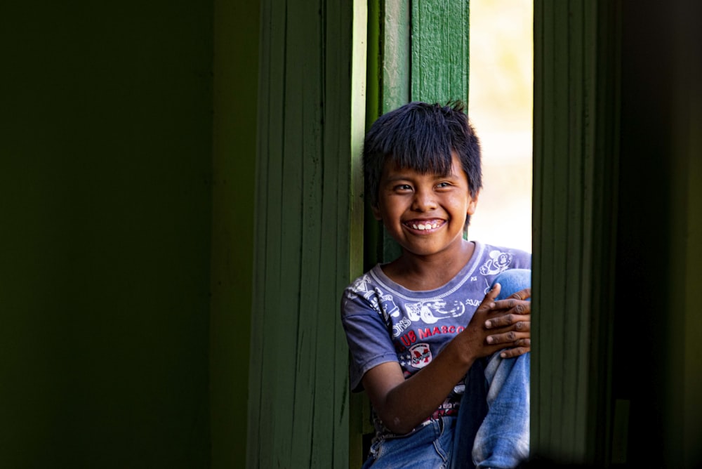 Un garçon souriant et appuyé contre une fenêtre