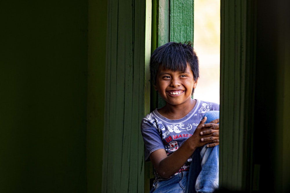 a boy smiling and leaning against a window