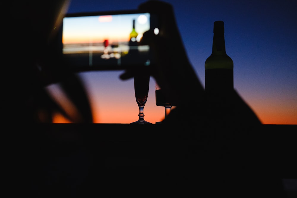 a silhouette of a person holding a bottle in front of a television