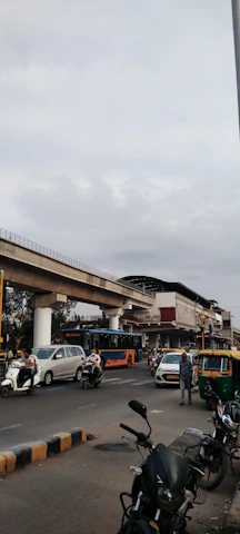 A bustling street scene in Delhi with people and vehicles under a cloudy sky.