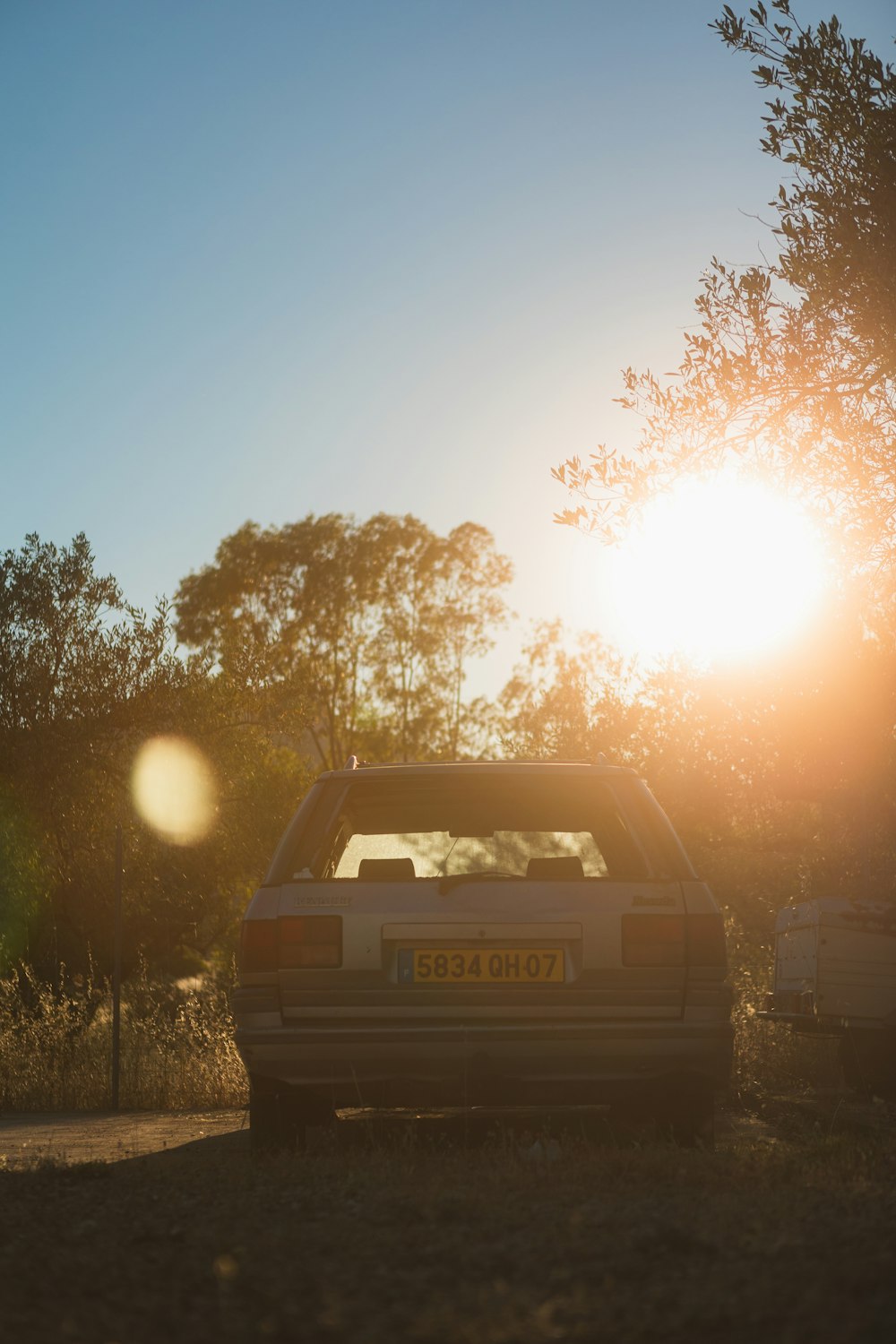 a car parked on a road with trees and the sun in the background