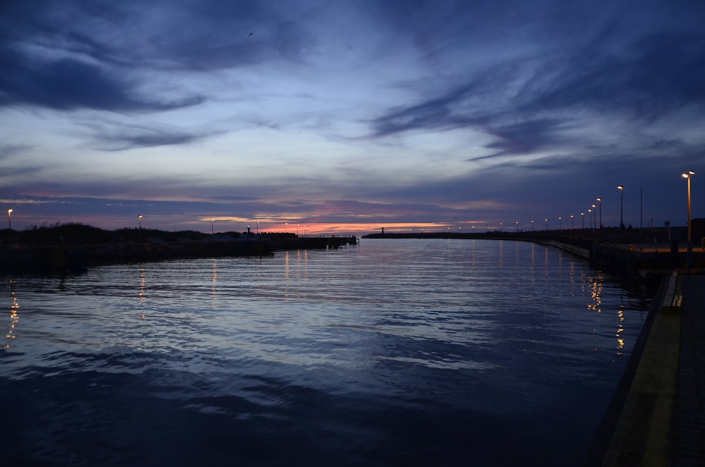 a body of water with a dock and a sunset in the background