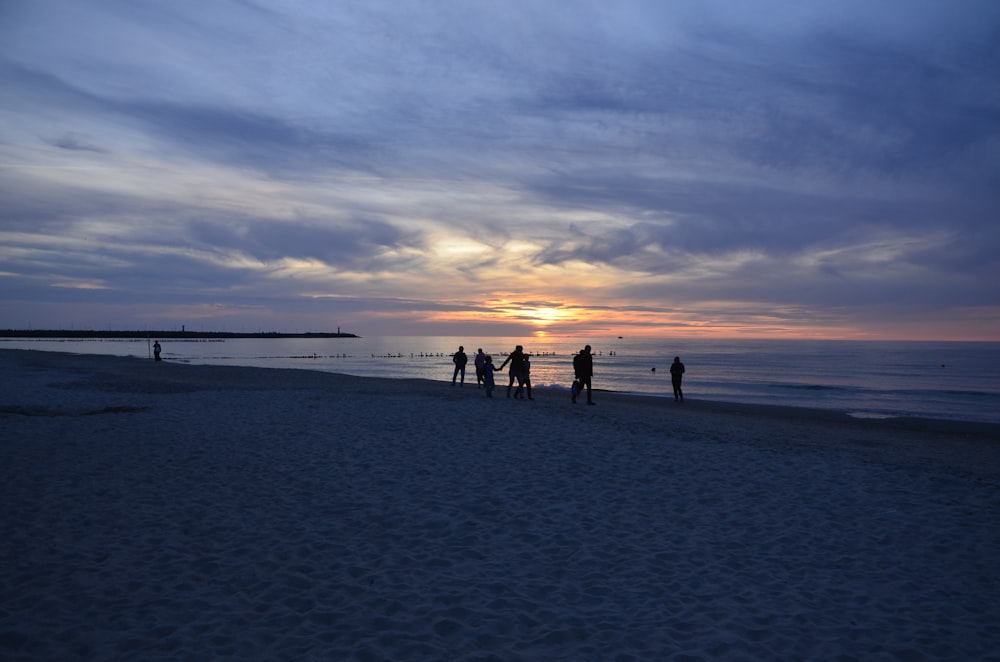 a group of people walking on a beach at sunset