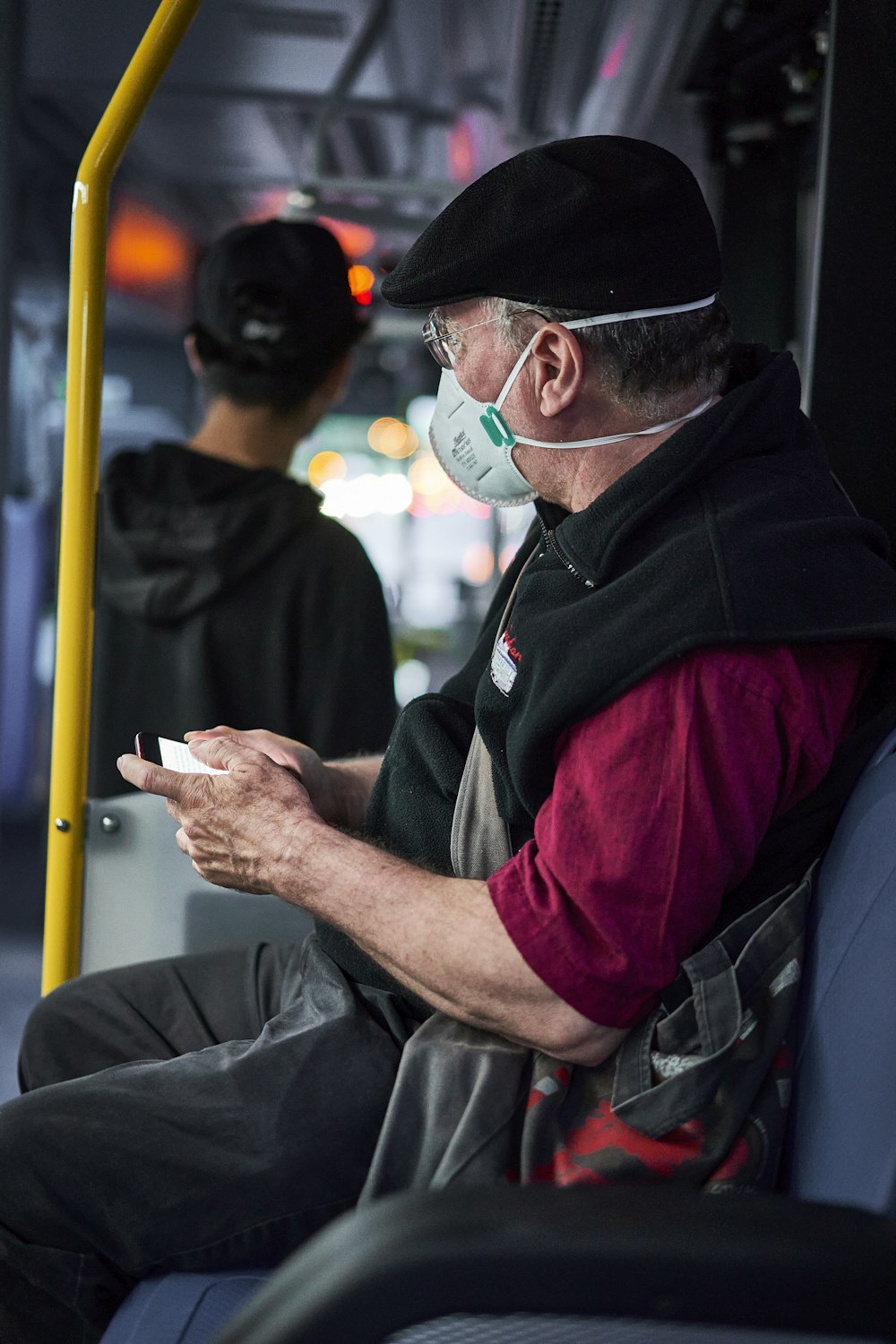 a man wearing a mask and a hat sitting on a bus