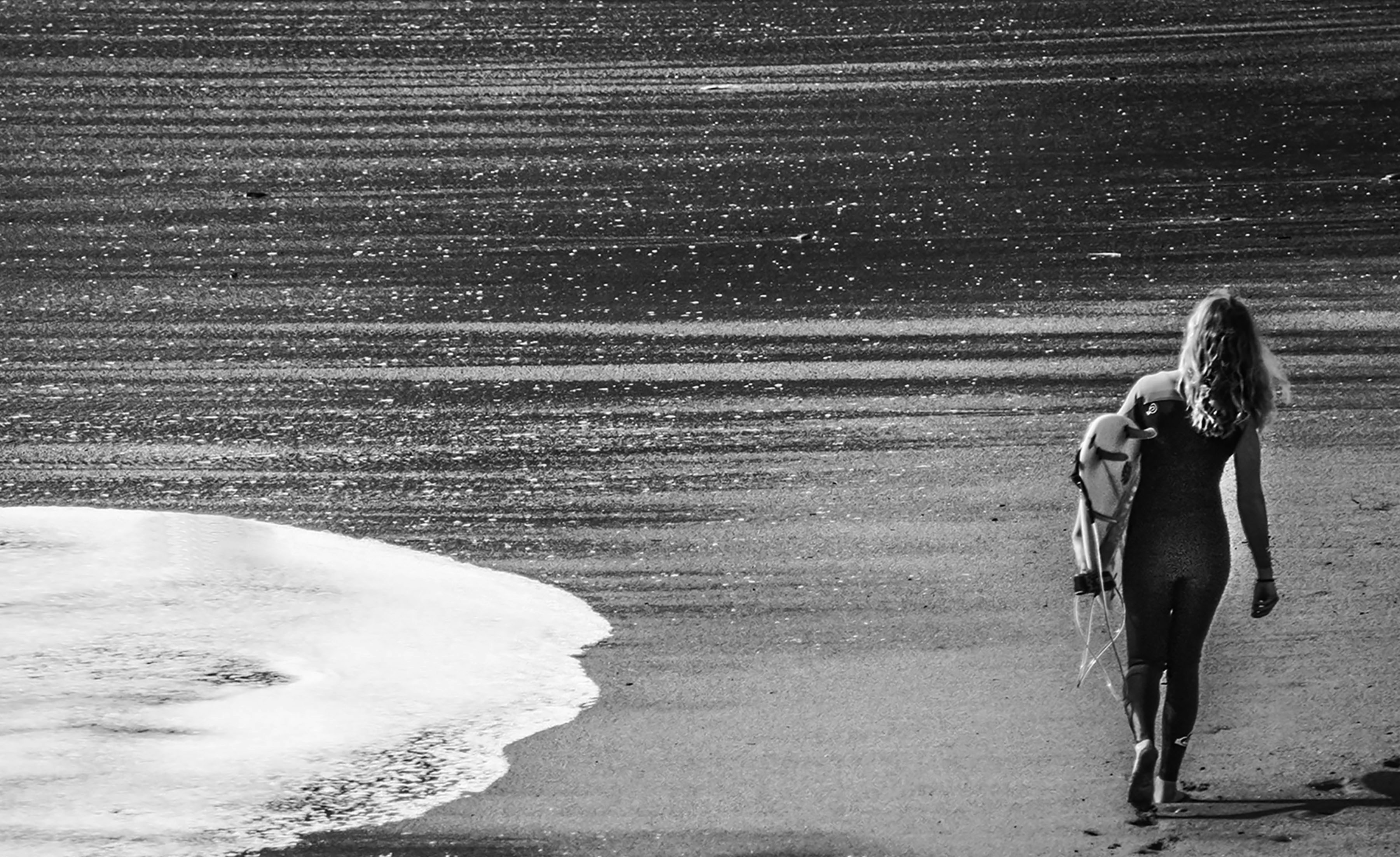 a couple of women walk down a beach carrying surfboards