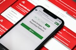 A smartphone displaying a rapid antigen test reporting platform application is placed on top of several red and white boxes labeled with 'Rapid SARS-CoV-2 Antigen Test.' The phone screen shows options for different languages and a start button for the application.