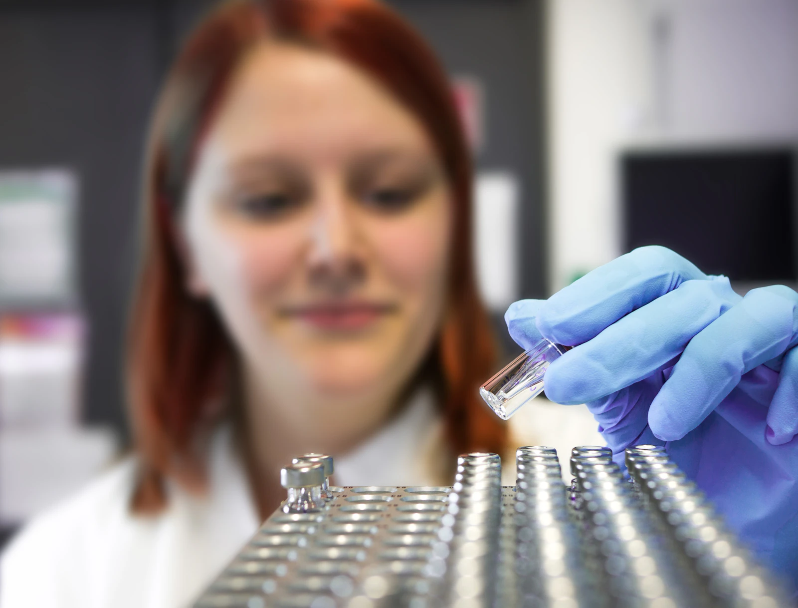 A woman researcher in a white lab coat working at a laboratory bench.