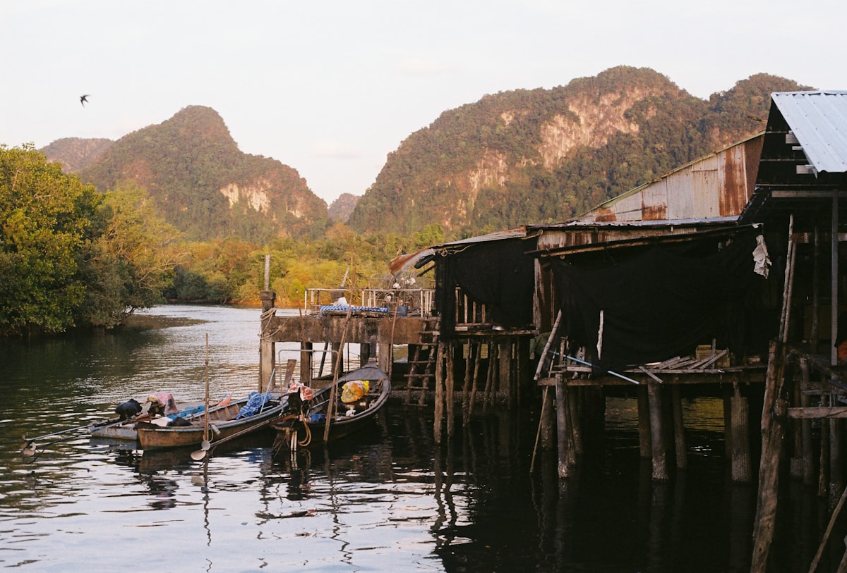 Krabi Town — stilted wooden fishing huts over the Krabi river estuary with limestone karst mountains behind, the provincial capital where actual Thais live