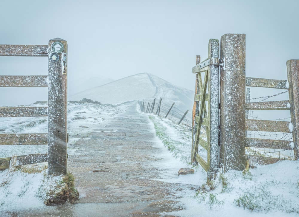 a snowy road with a fence and a wooden gate