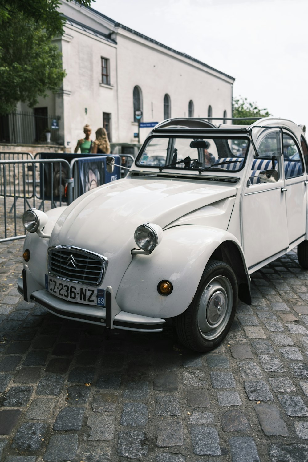 a white car parked on a brick road with people standing on the side