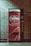 A vending machine with a bright red design featuring white text and decorative bubbles. It has the branding 'Drink Cheerwine Bottling Company' prominently displayed. The machine is set against a tiled wall in a dimly lit area.