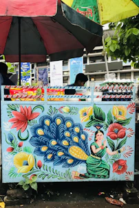 A colorful food stall adorned with intricate Madhubani paintings, showcasing steaming plates of Indian street food.