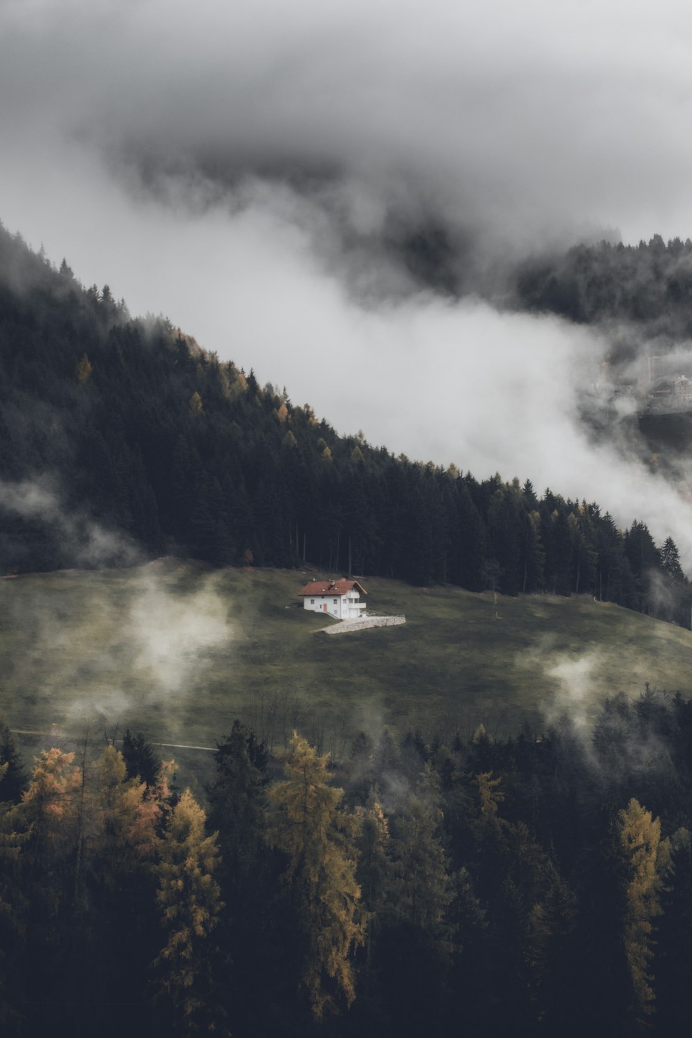 a house on a hill with trees and fog around it