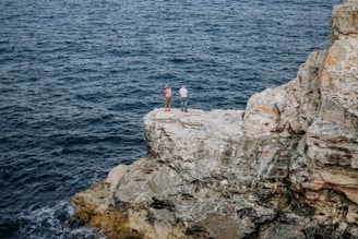 a couple of people standing on a rock by the water