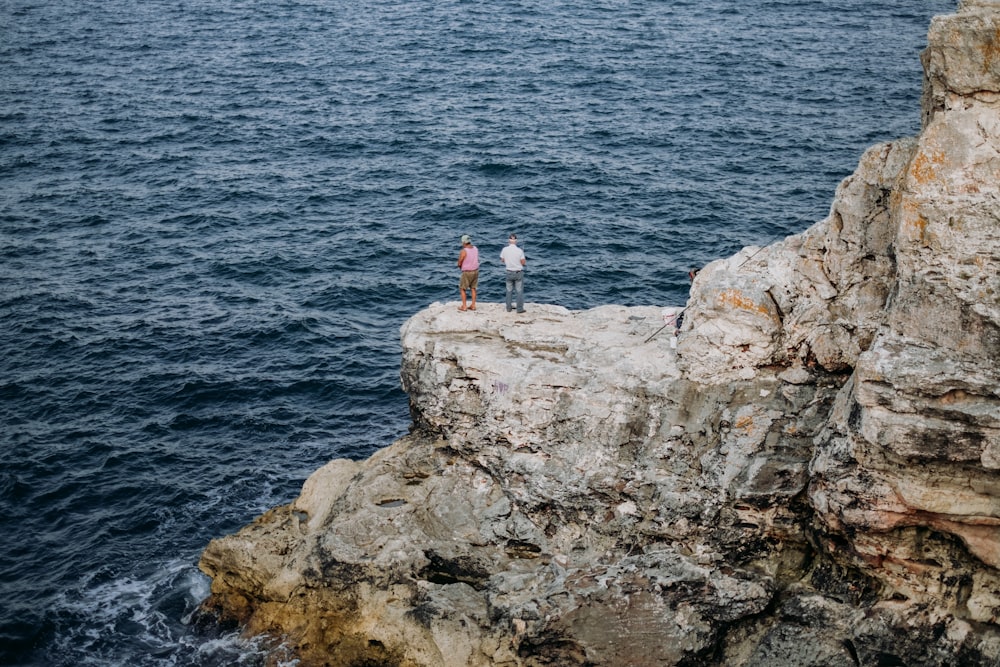 a couple of people standing on a rock by the water