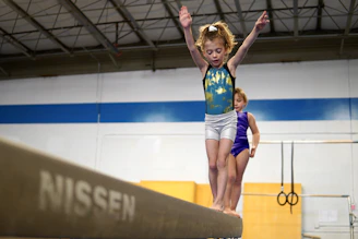 A gymnast performing on a balance beam in a well-lit gymnasium.