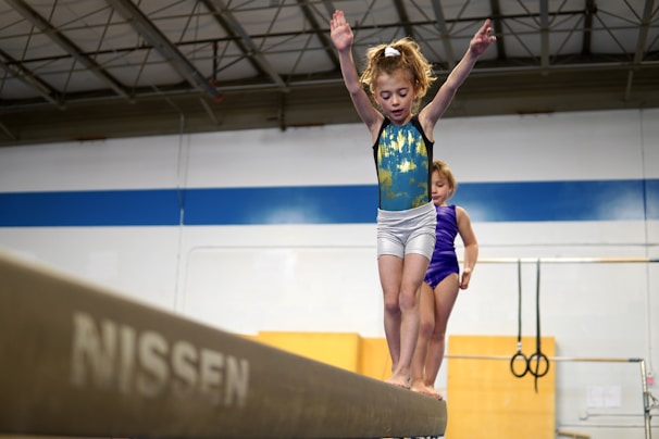 Young gymnast practicing balance beam in bright gym hall.