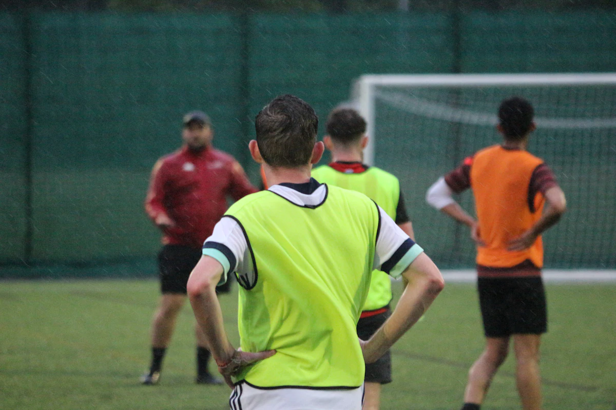 Adult players in training bibs wait for kick off on a wet evening