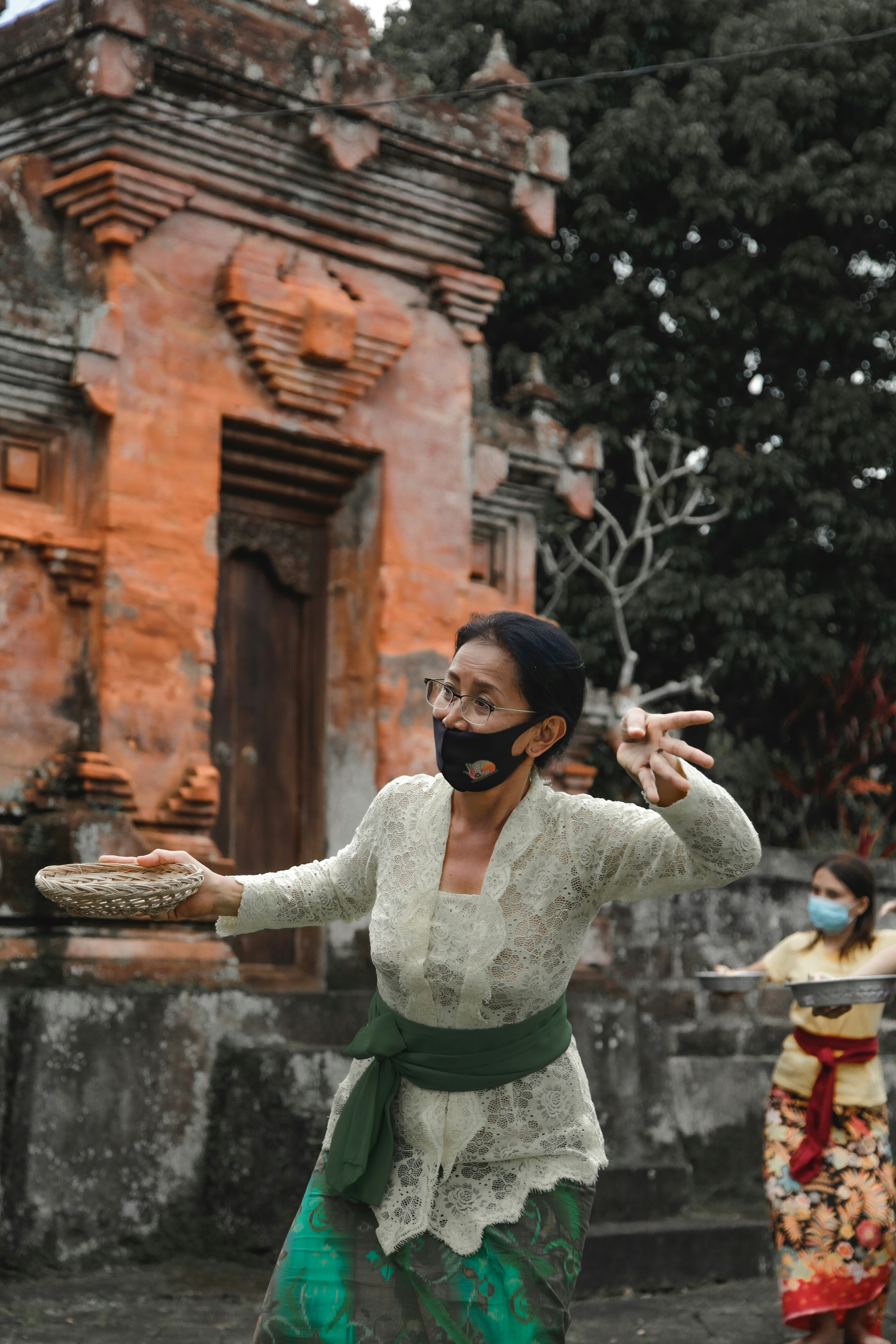Balinese woman in traditional attire, demonstrating a graceful dance gesture during a cultural lesson, with a serene temple background