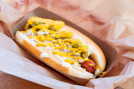 Close-up of a sizzling hotdog with mustard and onions on a soft bun.