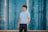 A person stands confidently in front of a backdrop of modern, glass skyscrapers. The individual is wearing a white shirt and dark pants, looking upwards with a contemplative expression.