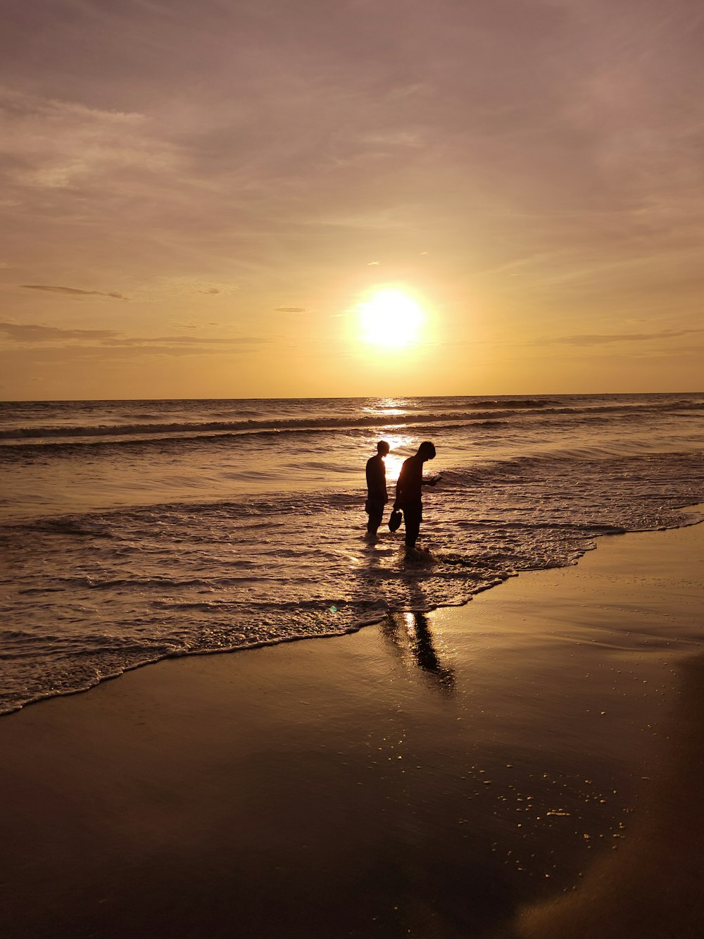 a couple of people standing on a beach with the sun setting