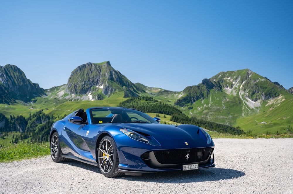 a blue sports car parked on a road with mountains in the background