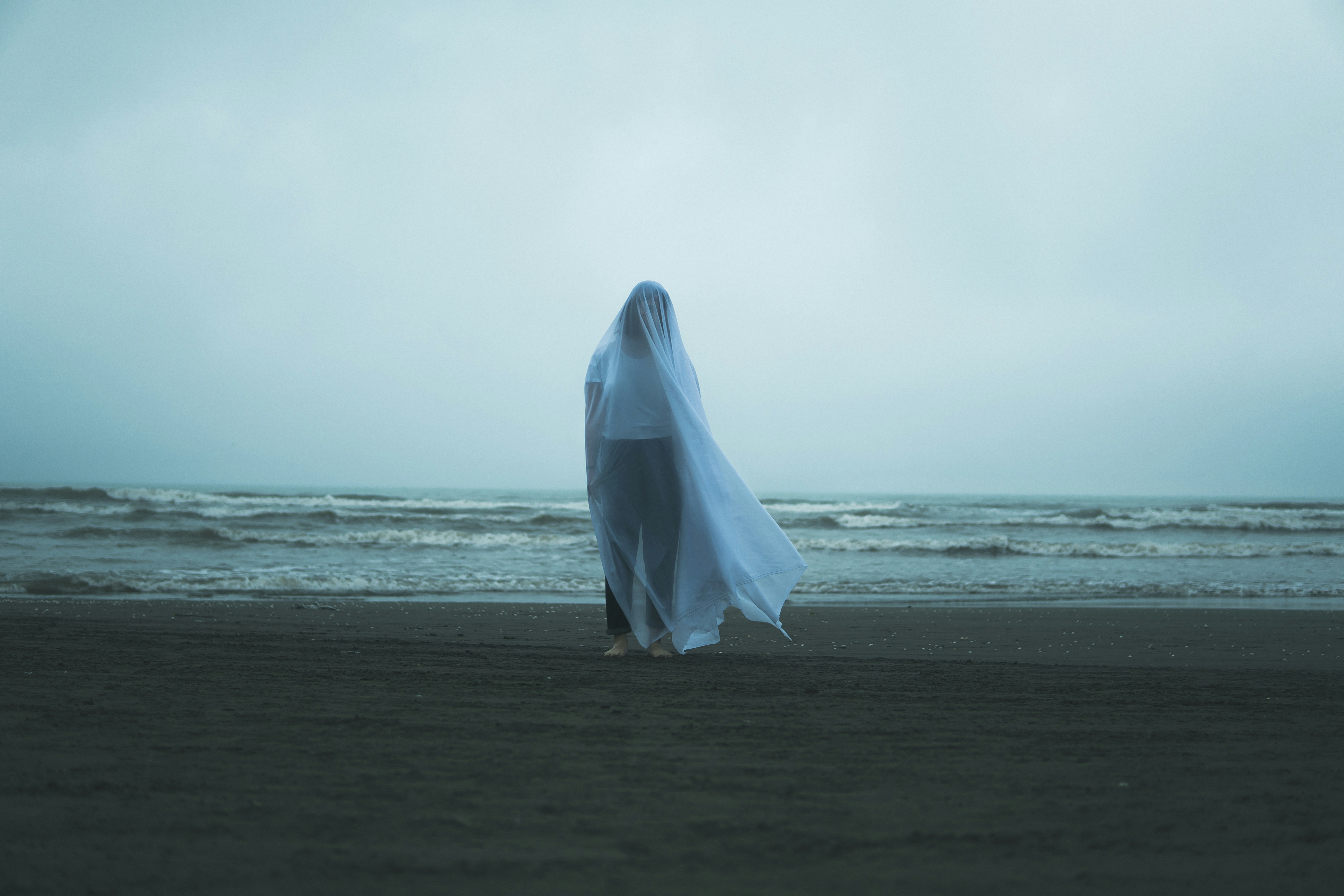 A person in a white sheet on a beach