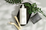 a white vase with a white candle and a plant on a white surface