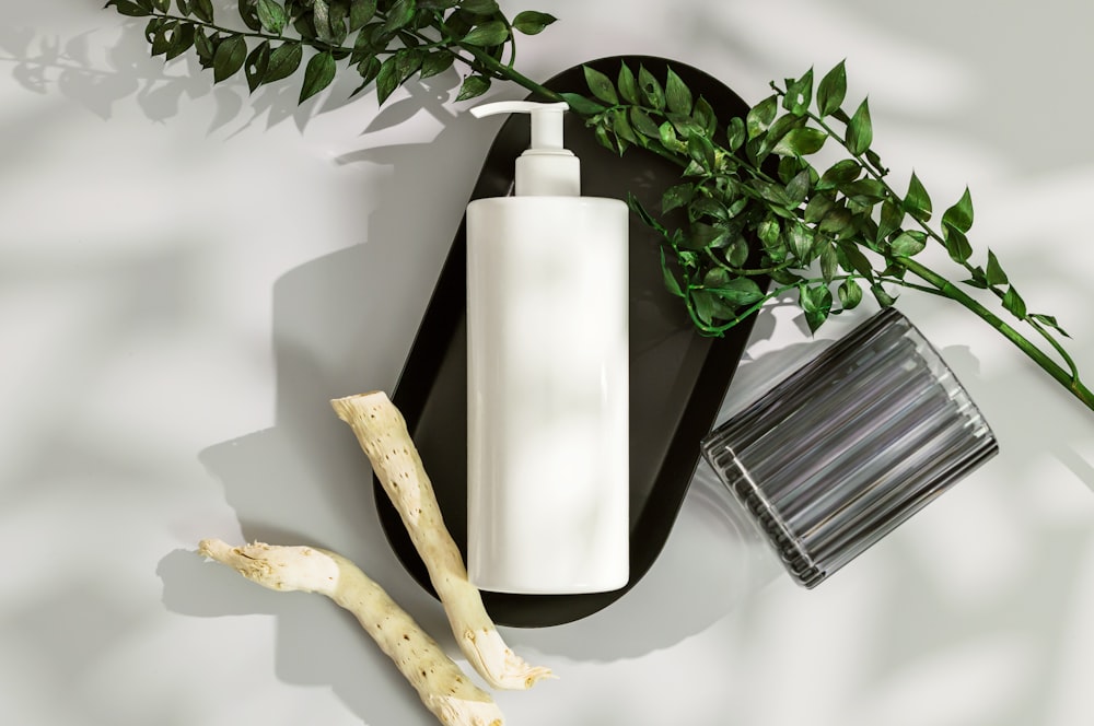 a white vase with a white candle and a plant on a white surface