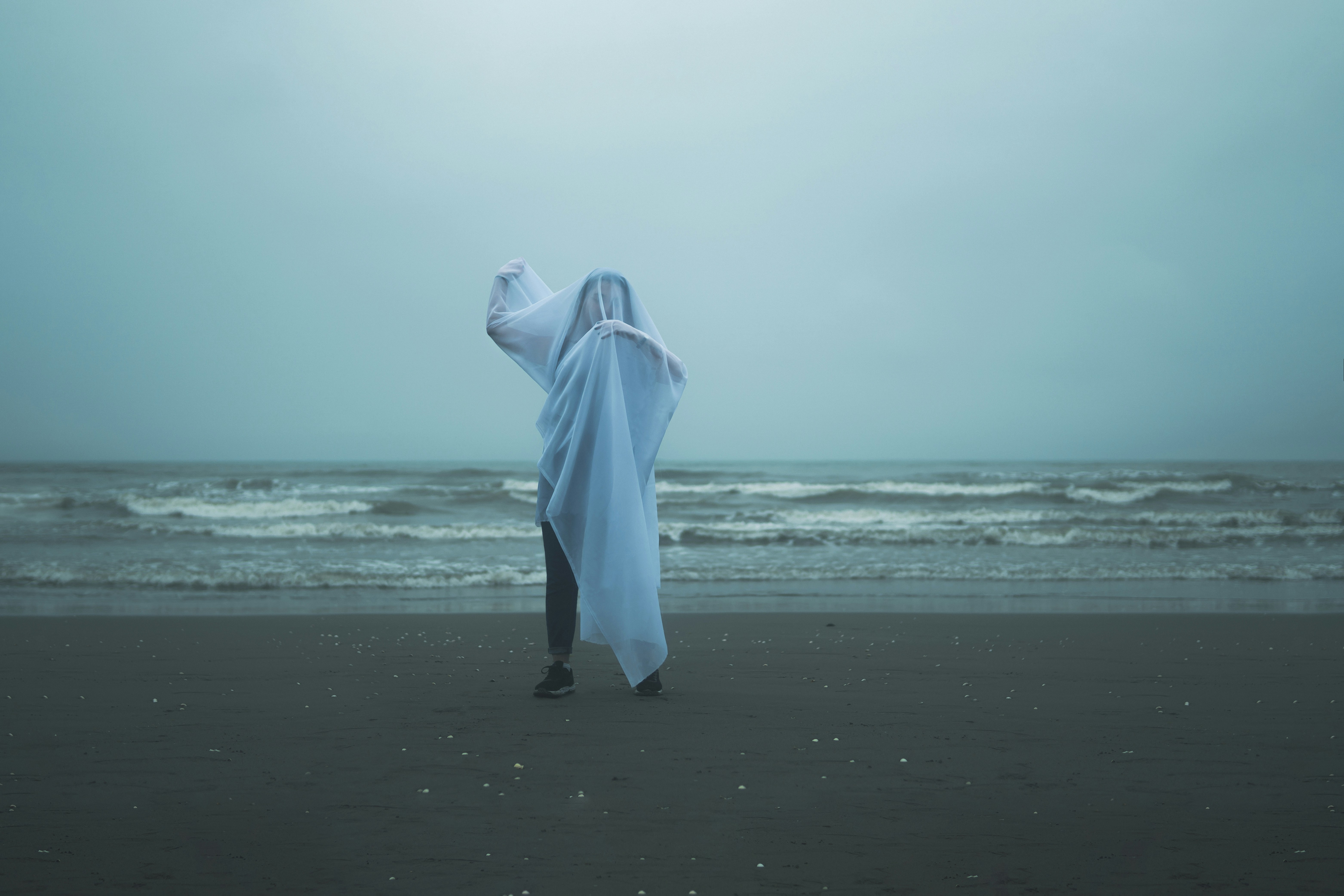 A person in a white sheet on a beach
