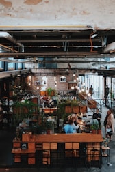 a person sitting at a table in a room with plants and people