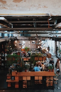 a person sitting at a table in a room with plants and people