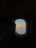 A calm sky at dusk viewed through an airplane window, highlighting serene blues and soft light.