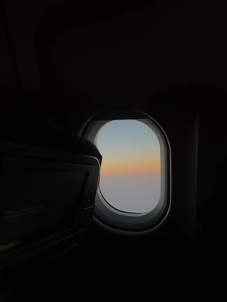 A calm sky at dusk viewed through an airplane window, highlighting serene blues and soft light.