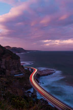 A dusk aerial shot of a winding coastal highway with sparkling city lights.