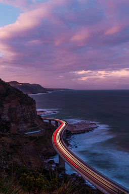 A dusk aerial shot of a winding coastal highway with sparkling city lights.