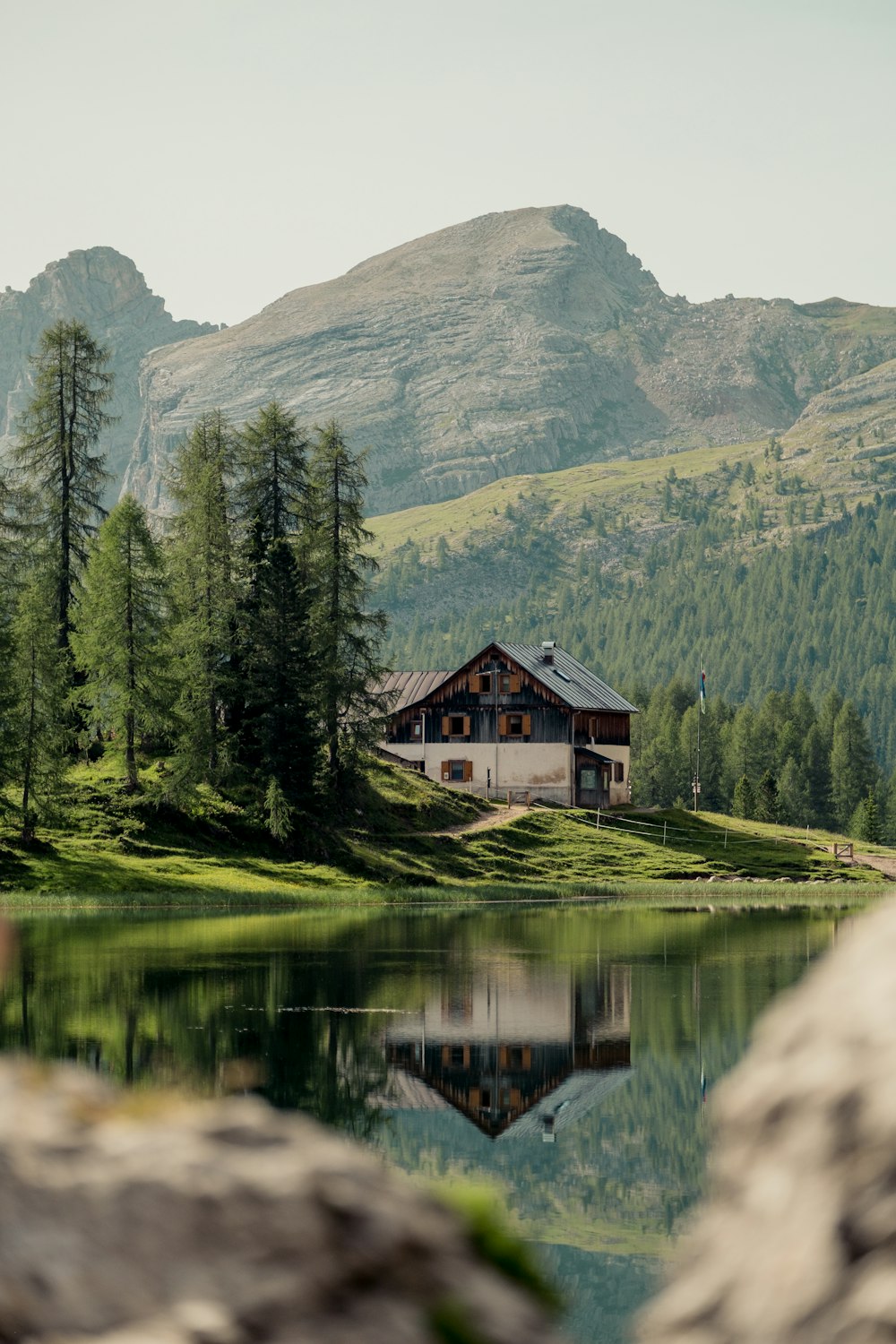 uma casa em uma colina à beira de um lago com árvores e montanhas ao fundo